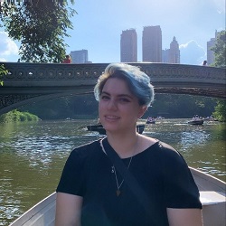 A photo of Lau in a canoe. In their background, there's a bridge and buildings peering out. Lau is wearing a black t-shirt. 