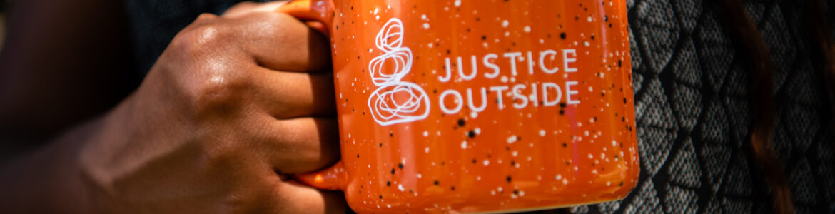 An orange mug with Justice Outside's white logo on it.