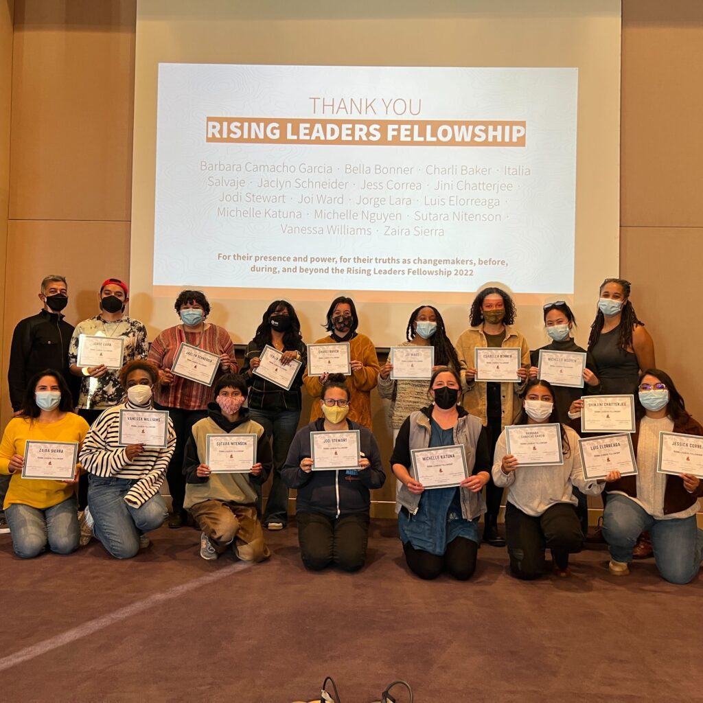 Sixteen people pose in front of a slide that reads Thank you Rising Leaders Fellowship in two rows. They are holding certificates and wearing face masks. 