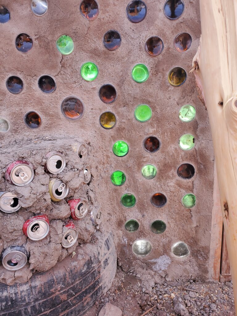 Glass and aluminum bottles and a tire being used for structure building by Kern and his team. 