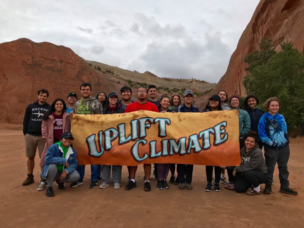 About two dozen people pose for a picture near orange hills. They hold a sign that reads "Uplift Climate."