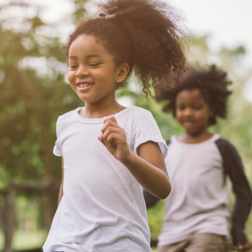 Two little Black children run outside. The one in the front is shown more clearly and smiling. 