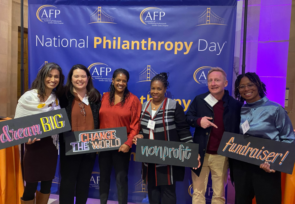 Image depicts Justice Outside staff members, a supporter, and a Board Member in front of the step and repeat for the National Philanthropy Day event held by the Association of Fundraising Professionals. The Justice Outside team is holding signs that read "dream big" "C