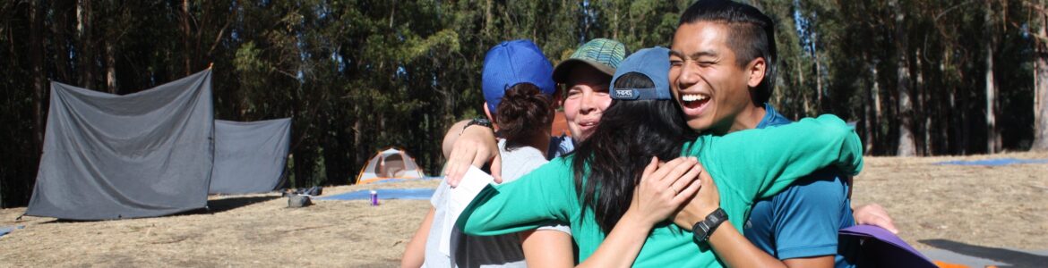 Four people hugging outdoors. There's a tent behind them.