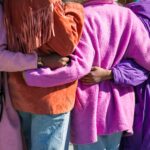 Four people in purple, pink, and orange coats standing outside embracing each other.