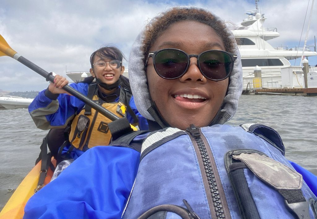 Two young people on a yellow kayak. They are wearing blue vests and jackets. 