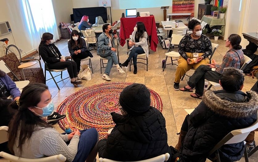 Members of Rising Leaders Fellowship in LA gather around in a circle and are engaged in conversations. Many folks are wearing masks and are people of color. 
